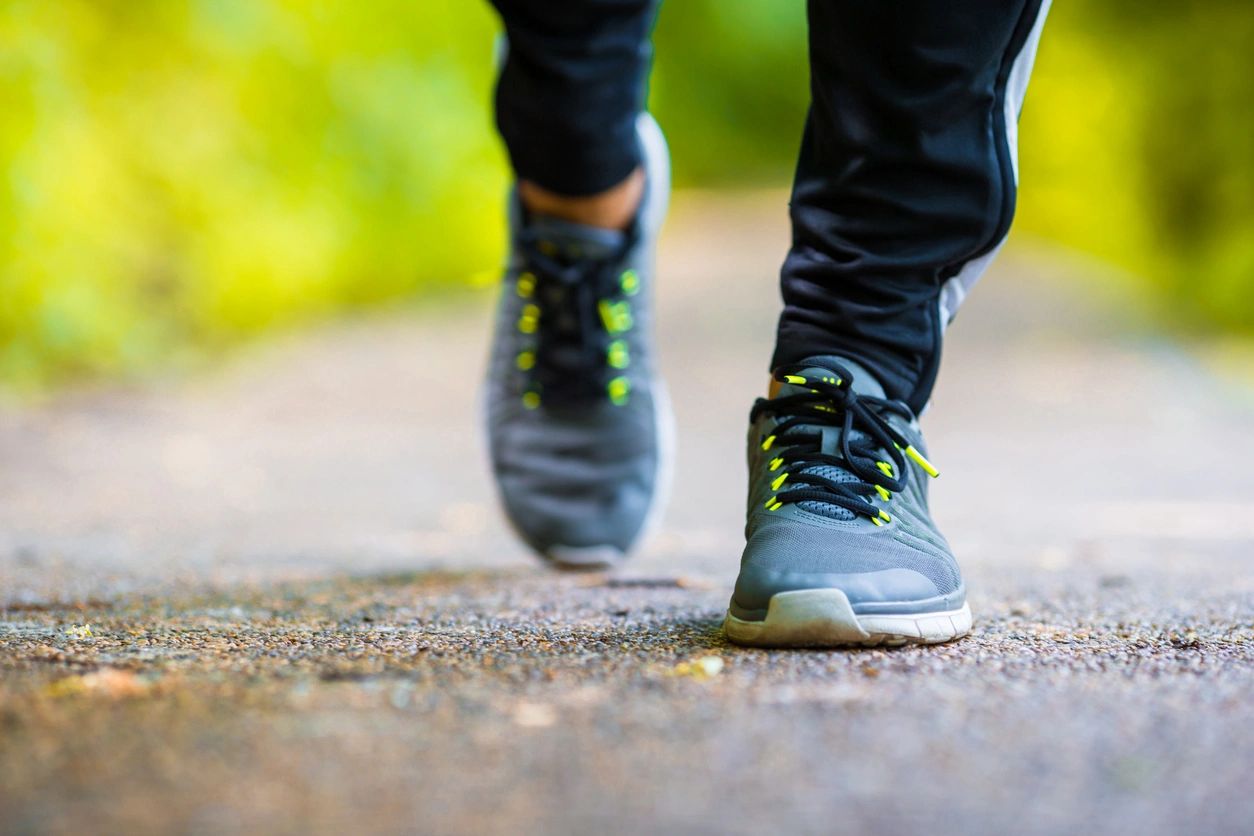 Close-up of someone jogging on a paved path wearing gray and green running shoes.