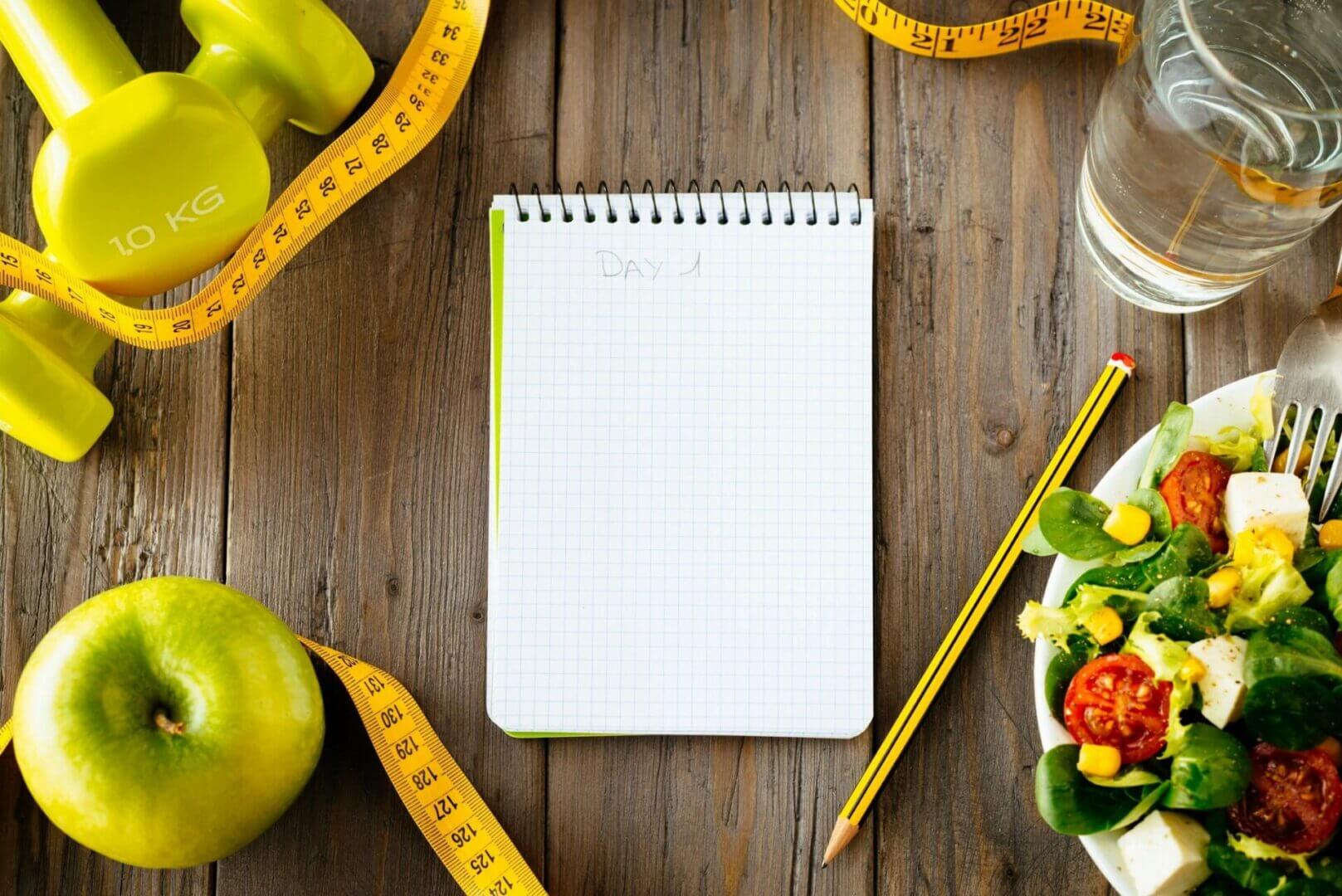 Blank notepad surrounded by fresh vegetables and a measuring tape on a wooden table.