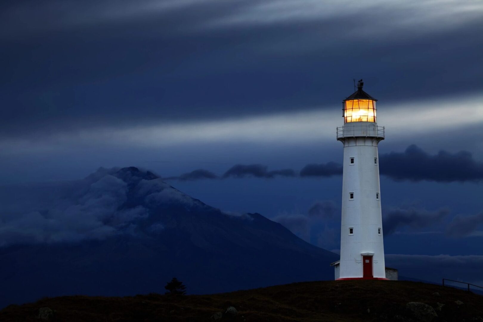 A glowing lighthouse stands against a dark, cloudy night sky.