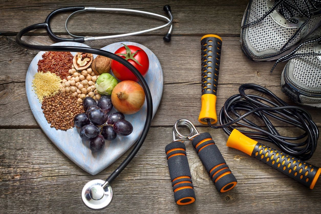Heart-shaped bowl with healthy foods and fitness gear including a stethoscope and jump rope.